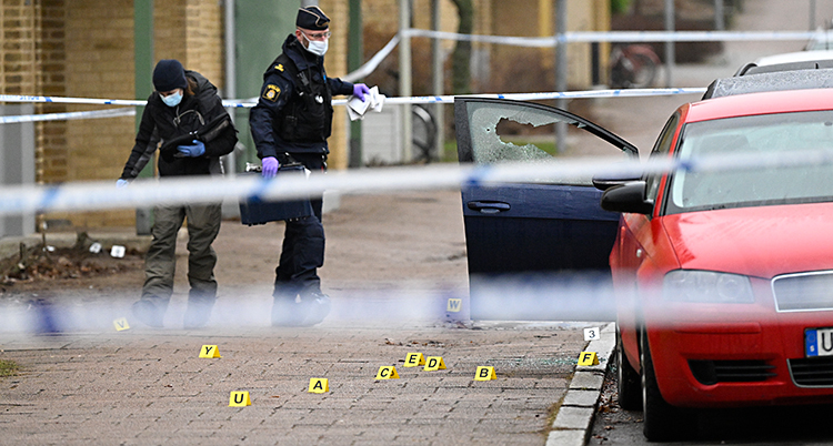 Två poliser står på en trottoar nära några bilar.