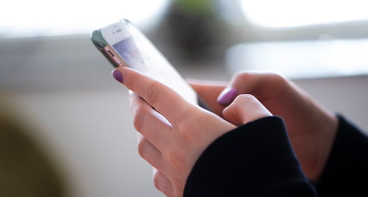 Ett par händer med rosa nagellack håller i en mobiltelefon.