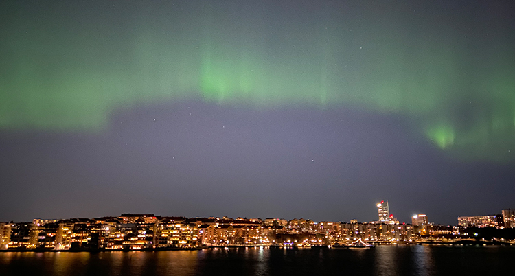 Himlen lyser upp i ett grönt ljus. Nedanför syns många hus och lägenheter.