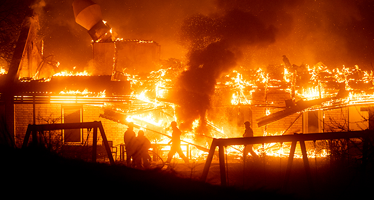 Det är natt. Det är stora lågor av eld och mycket rök från ett hus. Flera brandmän är vid huset.