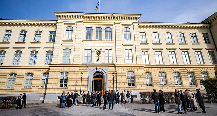 En bild på den stora skolan, utifrån. Flera människor står samlade utanför skolan.