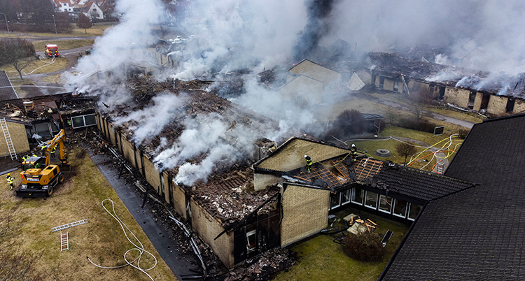 Fem utbrunna hus fotade ovanifrån. Det ryker från husresterna.