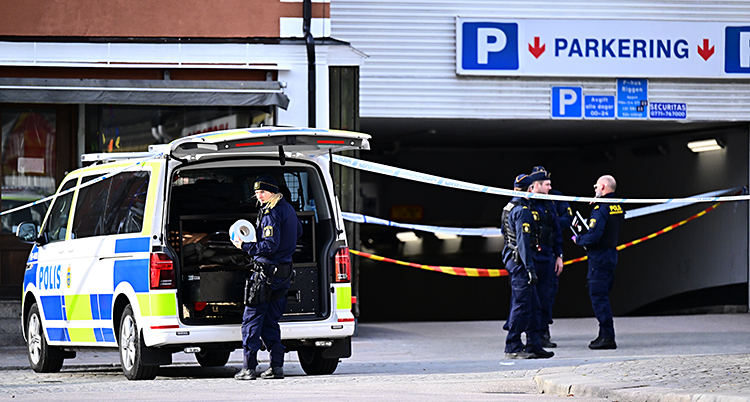 En polisbil står utanför ett parkeringsgarage. Flera poliser står där.