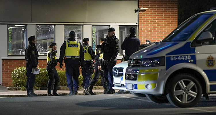 Det är kväll. Flera poliser står samlade på en parkeringsplats.