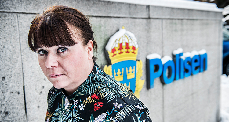 Hon tittar in i kameran. Hon står mot en vägg där det står Polisen.