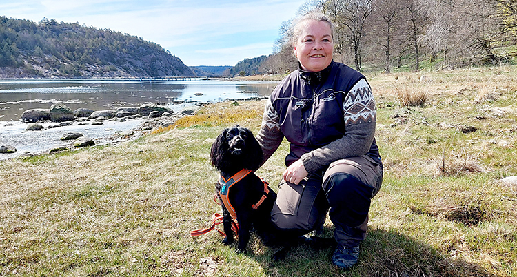 Hon sitter på knä i naturen bredvid en svart hund