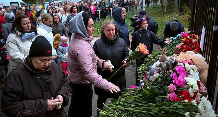 Hundratals människor är samlade vid grindarna till en skola. De lägger blommor vid grindarna.