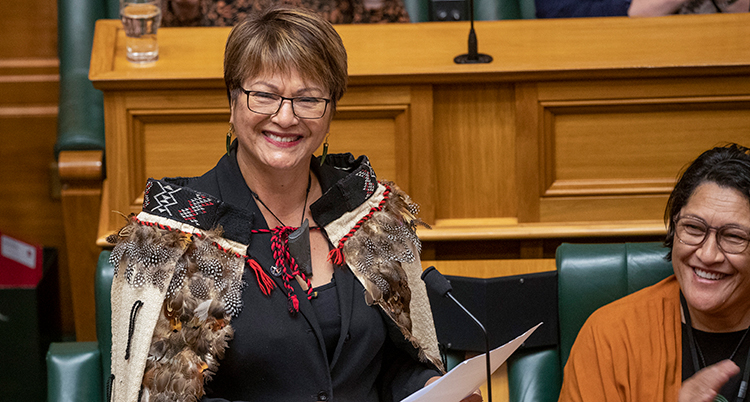 Hon sitter i en bänk i riksdagen. Framför finns en mikrofon. Nedför sitte ren annan kvinna.