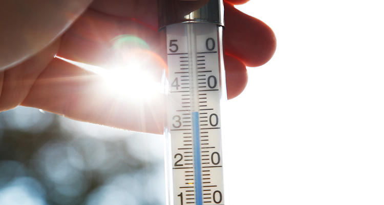 En hand håller i en termometer. Solen lyser i bakgrunden.