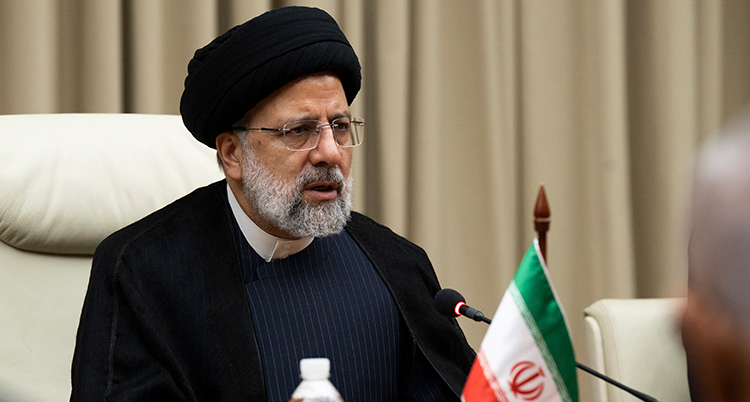 En äldre man i turban bakom ett bord med en iransk flagga.