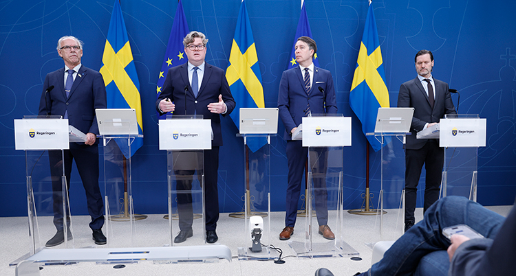 Fyra män står på rad. De har mikrofoner framför sig.