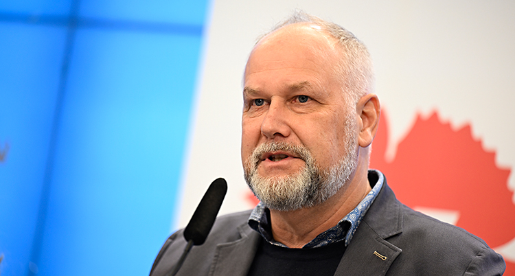 Han står och pratar i en mikrofon på en träff för journalister.