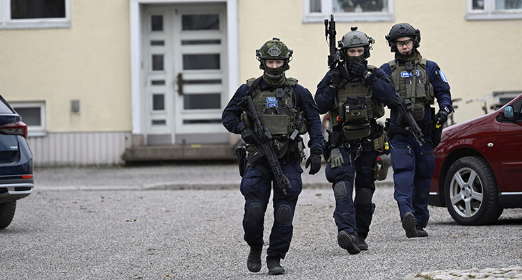 Tre poliser med vapen går på en skolgård.