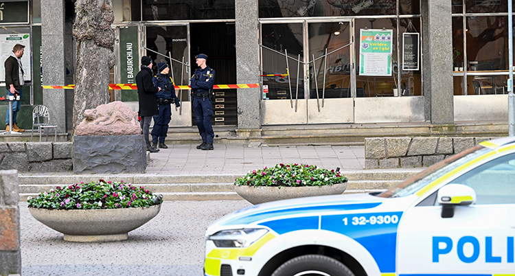 Tre poliser står utanför en ingång. En polisbil syns också lite.