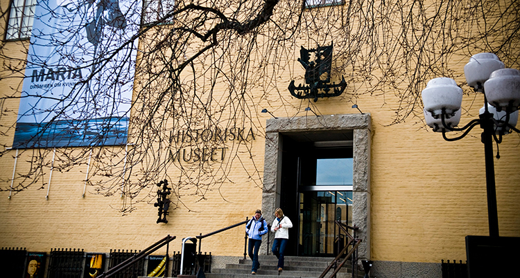 Ett ljusgult storthus. Två personer går nerför trappan vid entrén