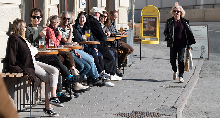 Flera människor sitter på rad på en uteservering i solen.