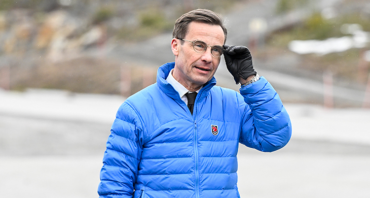 Ulf Kristersson står utomhus i en blå jacka. Han rättar till sina glasögon.