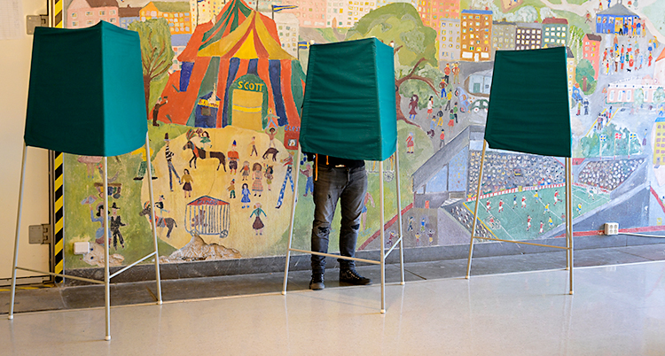 En person står dold bakom en grön skärm. Personen väljer vad den ska rösta på.