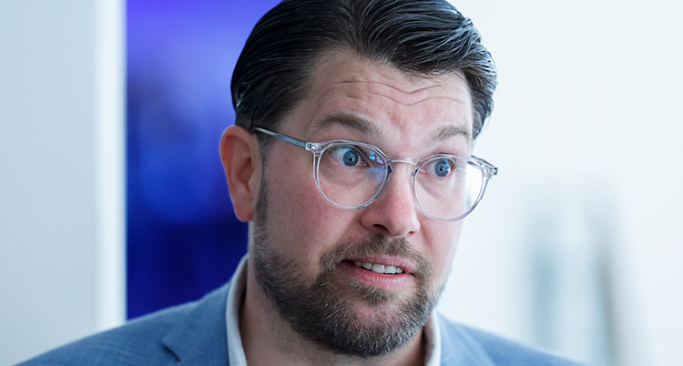 Han tittar på någon vid sidan om. Han har glasögon och kavaj.