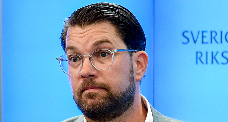 Han har glasögon och mörkt skägg.