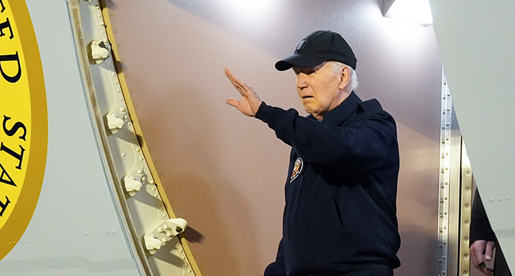Joe Biden står vid ingången till et flygplan och vinkar.