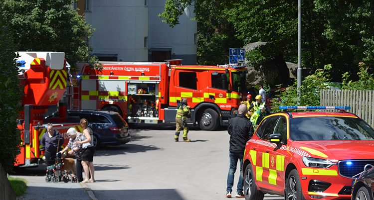 Flera brandbilar står framför ett högt hus. Personer går på gatan.