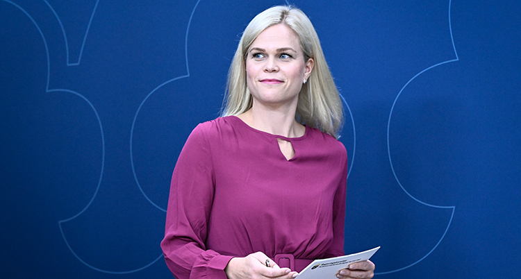 En halvkroppsbild. Hon har ljust långt hår och en rosa klänning. Hon håller i papper.