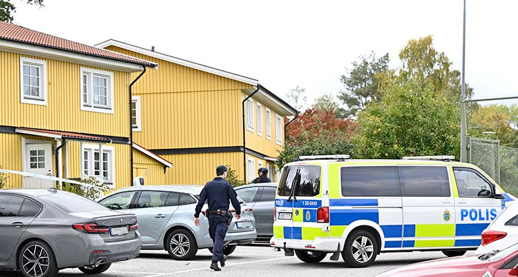 En polisbuss står på en parkering framför några gula hus.