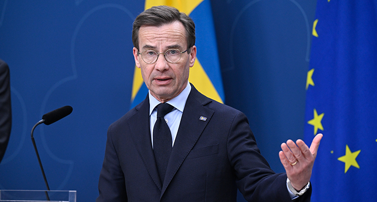 Man pratar i en mikrofon och sträcker ut en hand.