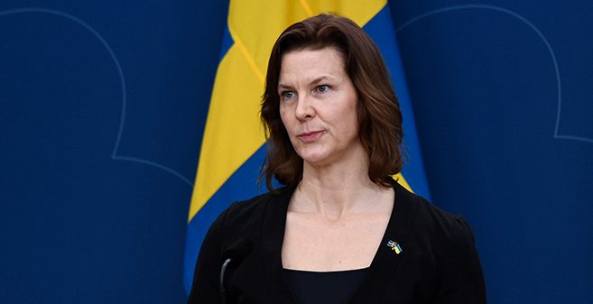 Hon står framför en svensk flagga på ett möte.