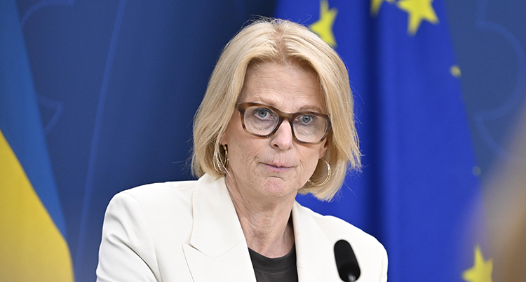 Hon är på ett möte med journalister. I bakgrunden syns svenska flaggor.