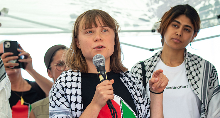 Hon pratar i en mikrofon. Hon har en palestinasjal över axlarna.