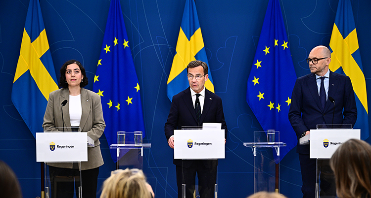 Statsministern står i mitten på en scen. De nya ministrarna står på varsin sida om honom.