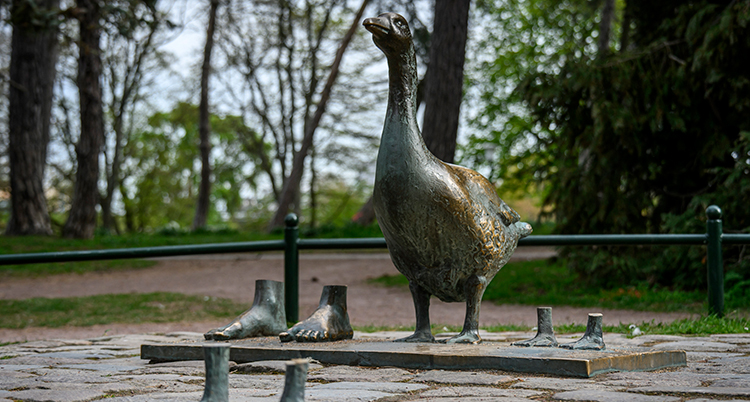 En staty av en gås syns i en park och bredvid den syns fötterna.