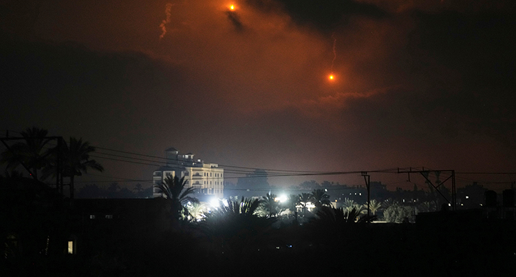 En bild på avstånd tagen på natten på hus i Gaza. I luften lyser två prickar upp den mörka himlen.