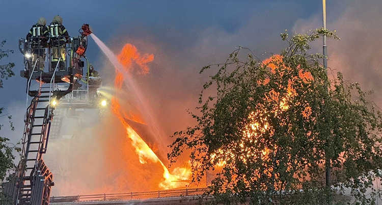 Brandmän står på en steg och sprutar vatten mot huset som brinner.