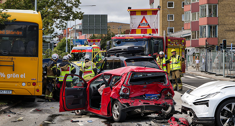 Brandmän jobbar vid olyckan. Två bilar är trasiga. Bussen står vid sidan av vägen.