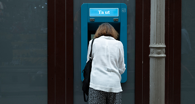 En kvinna står vid en bankomat och tar ut pengar.