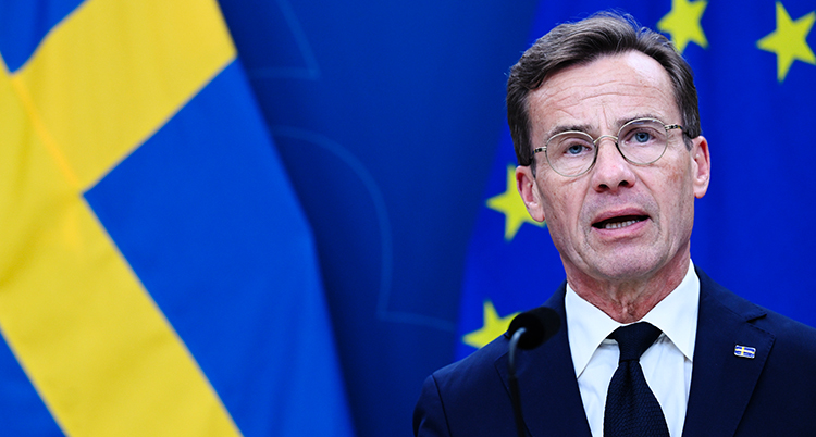 Han pratar på ett möte för journalister. I bakgrunden syns en svenska flagga.