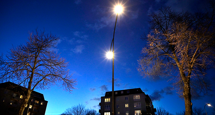 Skymning vid några hus. Två lampor lyser mot himlen.