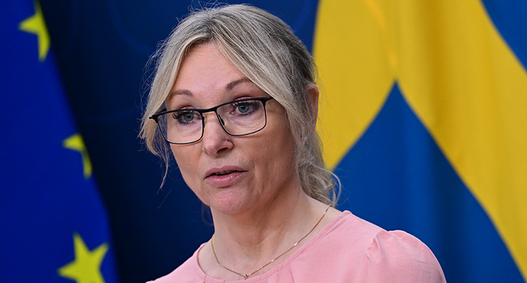 Hon står framför två flaggor, den svenska och Europeiska unionens.
