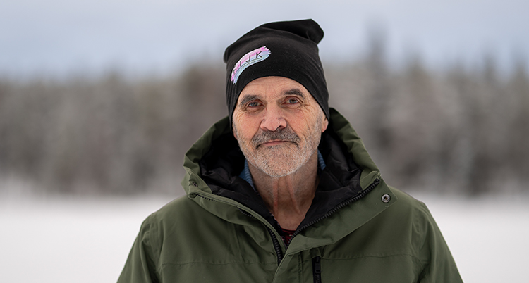 Ett porträtt. Han står utomhus. Han har mössa och jacka.