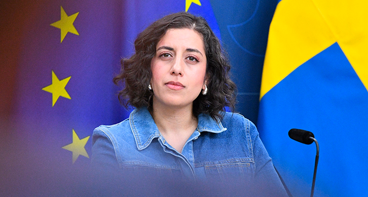 Hon står bakom en mikrofon och två flaggor, Europeiska unionens och Sveriges.