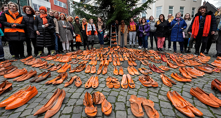 Många orangea skor står på marken. Kvinnor står bakom.