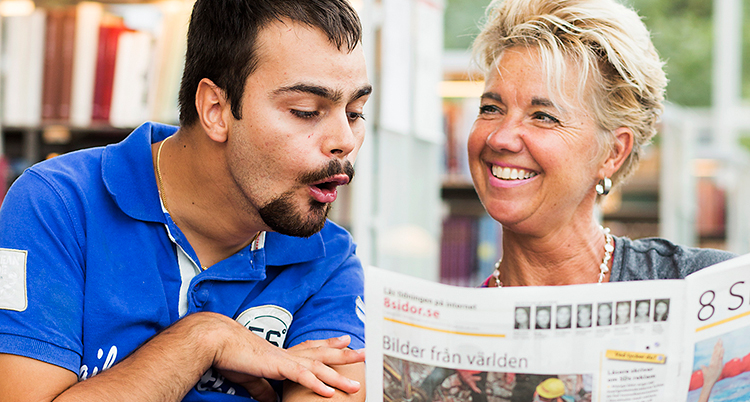 Två personer sitter bredvid varandra. De tittar i 8 Sidor. Hon håller upp tidningen.