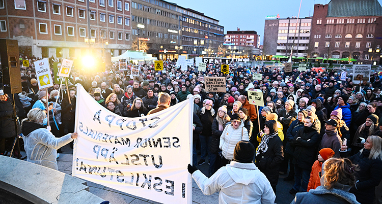 De står på ett torg. Många har skyltar.