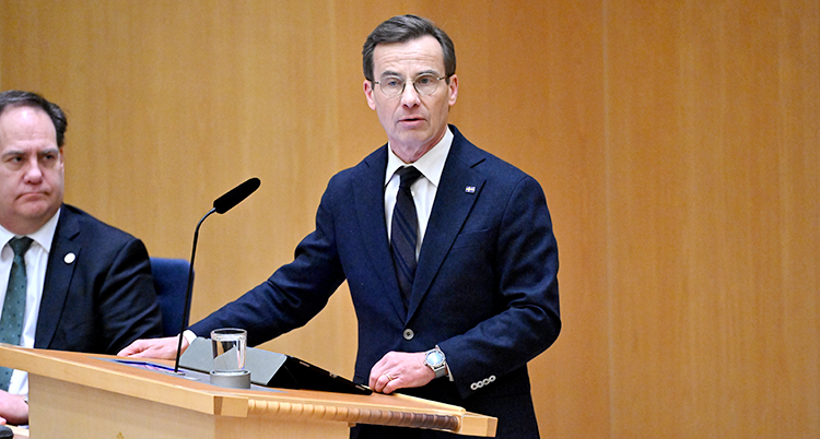 Ulf Kristersson står och pratar i mikrofonen i talarstolen i riksdagen.