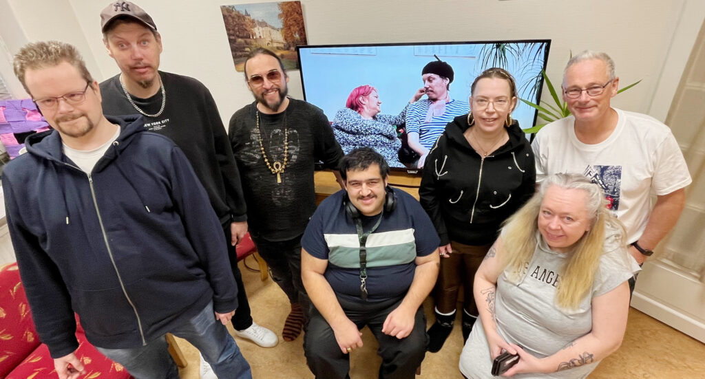 En grupp personer står och sitter framför en tv som visar en film.