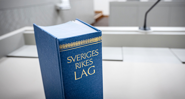 En blå bok står på ett bord. På bokens rygg står det Sveriges rikes lag.