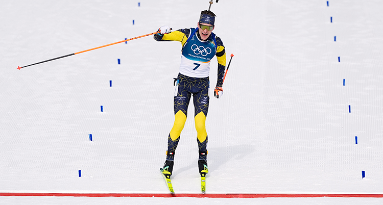 Från ett lopp i skidskytte. Martin Ponsiluoma åker över mållinjen. Han ser glad ut och sträcker ena armen i skyn.